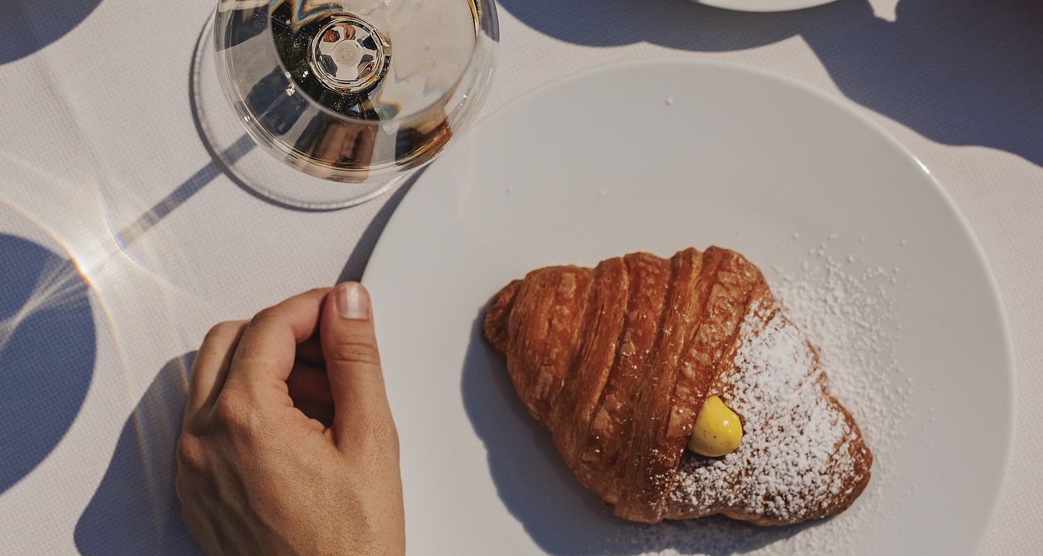 Una persona mangia un croissant al tavolo della colazione