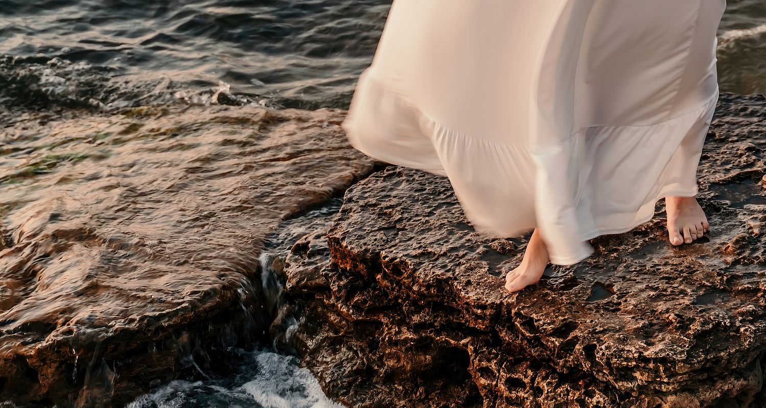 Donna con abito bianco a piedi nudi su una pietra e accanto il lago di Garda